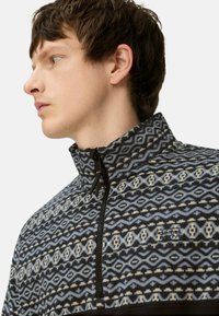 Fleecepullover med høj krave, der har et geometrisk mønster i nuancer af blå, sort og cream. Inkluderer en foran lynlås og logoaccent.
