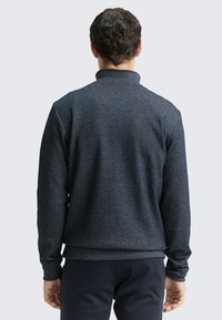 Donkergrijze trui met een hoge kraag, lange mouwen en een aansluitende zoom. Zachte, gestructureerde stof met een subtiel gemêleerd patroon.