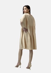 Pfirsichfarbendes, knielanges Kleid mit lockerer Passform, kurzen Ärmeln, strukturiertem Stoff und Nahtdetails; kombiniert mit beigen High Heels.