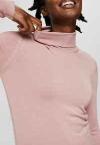 Jasnoróżowy sweter z golfem wykonany z miękkiej tkaniny, z prążkowanym wykończeniem kołnierza i bocznymi detalami dodającymi tekstury oraz atrakcyjnego wyglądu.