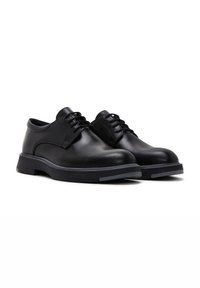 Zapatos de cuero negro con acabado suave, puntera redonda y cordones. Suela de goma gruesa con un ligero acento gris a lo largo del borde.