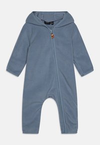 Lyseblå fleece overalls med hette, med lange ermer, glidelås foran og brun skinnaccent. Myk, teksturert stoff.