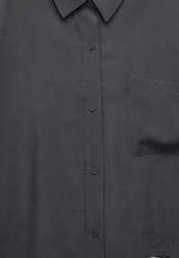 Chemise boutonnée gris foncé avec col et poche poitrine, présentant des coutures visibles et des boutons noirs sur le devant.
