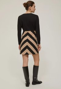 Abito a maniche lunghe con parte superiore nera e gonna beige con strisce a zigzag nere. Indossato con stivali neri fino al ginocchio. Texture liscia.