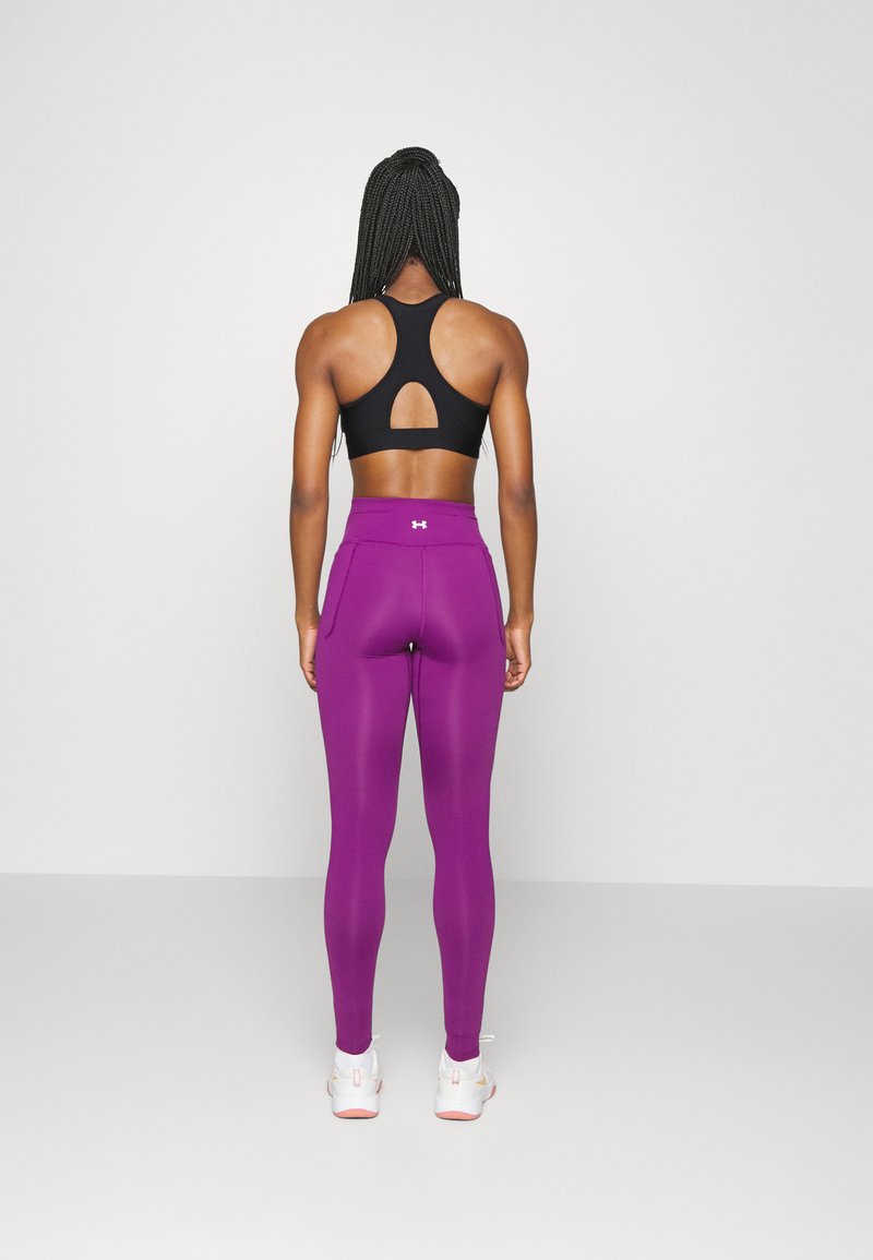 Sujeta negra con diseño de espalda nadadora y detalle recortado. Leggings morados ajustados con cintura alta y un acabado texturizado. Zapatillas blancas con acentos en rosa.