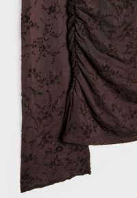 Smeđa tkanina s reljefnim cvjetnim uzorkom, s nabranym detaljima s jedne strane i glatkom završnom obradom s druge strane.