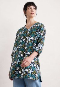 Tunika z dekoltem w kształcie litery V w kwiatowy wzór w zielonym, niebieskim i białym kolorze na ciemnym tle; rękawy trzech czwartych; luźny krój; boczne rozcięcia; tkanina o fakturze.