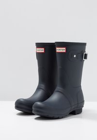 Bottes de pluie en caoutchouc noir avec logo "HUNTER" rouge et argent, détail de boucle sur le côté, semelle texturée et finition lisse et brillante.