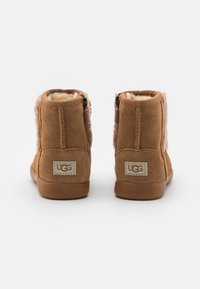 Brązowe zamszowe botki za kostkę z wyściółką z sztucznego futra, z suwakiem z boku i naszywką z logo UGG z tyłu. Taneczne gumowe podeszwy.