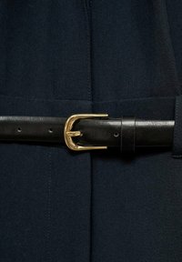 Svart läderbälte med en guldfärgad spänne, som har en slät yta och flera hål för justering, placerat runt en mörk tyg.