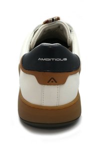 Zapatilla blanca con tacón azul oscuro, acento marrón y suela de goma texturizada. Logo "AMBITIOUS" en el talón. Presenta detalles de costura.