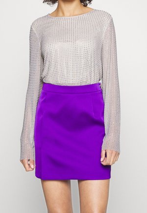 Przezroczysty srebrny top z detalami ze srebrnych cyrkonii, w połączeniu z jednolitą fioletową mini spódnicą o gładkiej fakturze i dopasowanym kroju.