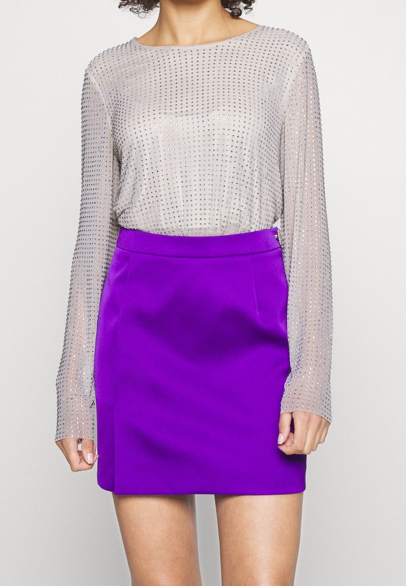 Haut en argent transparent avec des détails en cristaux de rhinocéros argentés, associé à une mini-jupe violette unie, avec une texture lisse et un design ajusté.