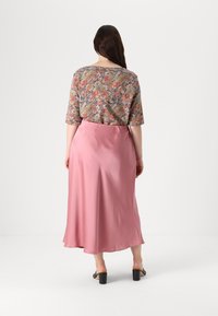 Haut à motifs floraux avec des manches courtes, associé à une jupe en satin rose fluide, longueur chevilles avec une texture lisse et une légère brillance.