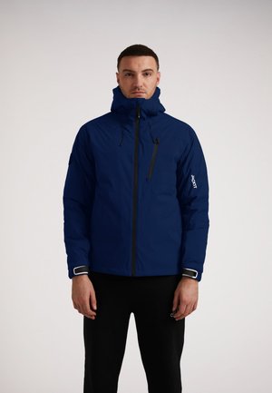 Marineblau wasserfeste Jacke mit hohem Kragen, verstellbarem Kapuzen und Reißverschlusstasche auf der Brust. Besitzt elastische Bündchen und ein Logo auf dem Ärmel.