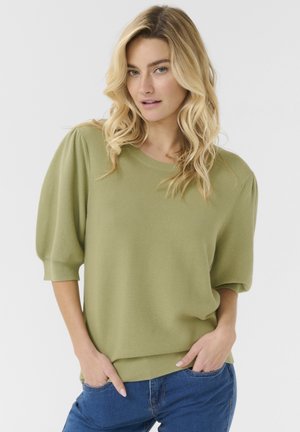Hellgrüner Strickpullover mit rundem Halsausschnitt und kurzen, puffigen Ärmeln. Mit geripptem Saum und Bündchen. Kombiniert mit blauen Jeans.