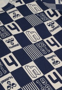 Materiał w kolorze granatowym i kremowym w wzory z cyframi, paskami oraz logo "hummel". Tekstura wydaje się gładka i przypomina bawełnę.