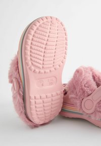 Zuecos de piel sintética rosa con suela de goma texturizada, que cuentan con una franja multicolor en el lateral y un detalle de botón para el cierre.