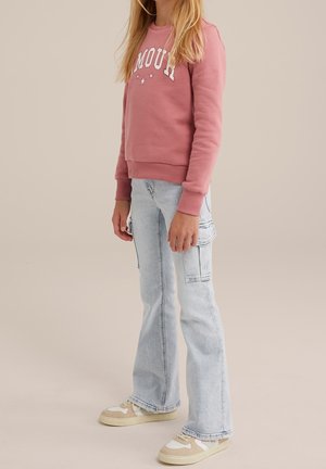 Sweat-shirt rose avec texte "AMOUR" blanc et étoiles, associé à un jean cargo évasé bleu clair et des baskets beige avec des accents en maille.