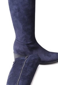 Bottes en suède bleu marine hauteur genou avec une texture lisse, un petit talon et un détail de fermeture éclair sur une botte.