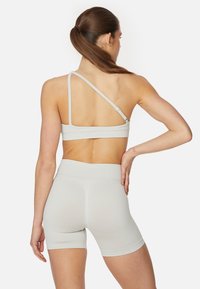 Lichtgrijze sportbeha met een kruiselings rugontwerp, gecombineerd met bijpassende aansluitende shorts. Het materiaal lijkt rekbaar en glad.