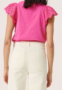 Top de algodón rosa con mangas de encaje, combinado con jeans de tiro alto color crema que cuentan con dos bolsillos traseros y una textura suave.