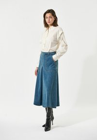 Bela srajca s gumbi, modre denim culotte s stranskimi žepi in črne čevlje na visoki peti. Gladko blago, krojena zasnova in sproščen kroj.
