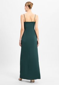 Maxikleid aus tiefgrünem Stoff. Verfügt über dünne Träger, ein eng anliegendes Oberteil und einen geraden Rock mit einem verdeckten Reißverschluss im Rücken.