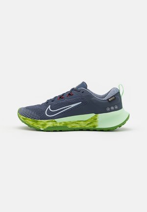 Baskets de course avec une tige en mesh bleu marine, une semelle texturée verte et des accents réfléchissants. Comprend des lacets rouges et un logo sur le côté.