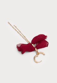 Delicate gold chain necklace with a red fabric bow and a small open gold hoop pendant on a white background.