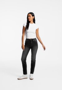 Černé džíny z denimu s slim fit, v kombinaci s přiléhavým bílým topem s krátkým rukávem a bílými teniskami. Jednoduchý design, bez viditelných vzorů.