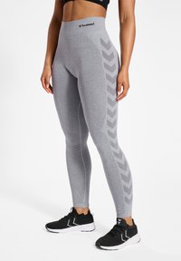 Jasnoszare legginsy z wysokim stanem, z wzorem w jodełkę po bokach. Połączone z czarnymi butami sportowymi.