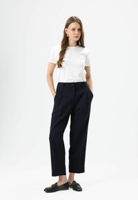 Witte top met korte mouwen en marineblauwe hooggetailleerde broek. De broek heeft een knoopsluiting en zijzakken. Zwarte loafers maken de outfit compleet.