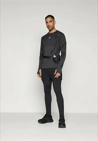 Schwarzes, feuchtigkeitsableitendes Langarmshirt mit reflektierenden Akzenten, kombiniert mit schwarzen Shorts und Leggings, inklusive einem Trinkgürtel.