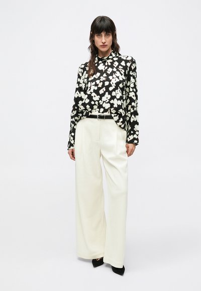 Czarna kwiecista koszula z długim rękawem, ozdobiona białymi i beżowymi kwiatami, zestawiona z szerokimi białymi spodniami i czarnymi szpilkami ze spiczastym noskiem.