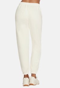 Witte, taps toelopende sweatpants met een elastische tailleband en boorden, gemaakt van zachte stof, gecombineerd met chunky witte sneakers.
