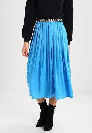 Mujer con falda midi plisada de color azul brillante con cintura elástica "PEPE JEANS", suéter negro y botines negros.