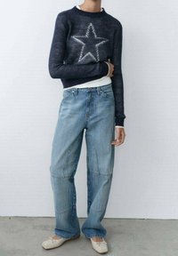 Marineblauwe trui met een wit sterontwerp, gecombineerd met lichtblauwe loszittende spijkerbroeken met stiksel details. Crème ballerina's met een afgeronde neus.