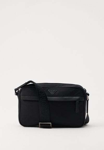 Sac à bandoulière en nylon noir avec une sangle contrastante, une forme rectangulaire élégante, un détail de logo et une poche zippée à l'avant.