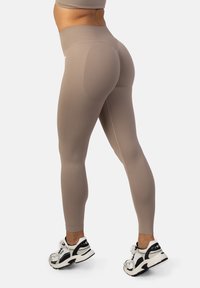 Béžové legíny s vysokým pásom, hladkej textúry a priliehavého strihu, skombinované s bielymi a čiernymi teniskami s robustným siluetou.