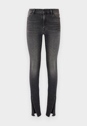 Top court en rib ou rouge avec des accents blancs et un branding, associé à un jean skinny gris foncé avec fentes sur les côtés et des baskets noires.