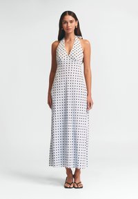 Šaty bez rukávov s halter výstrihom, vyrobené z ľahkej látky; sú pokryté čiernymi bodkami na bielom pozadí; dlhé až po zem s priliehavým korzetom.