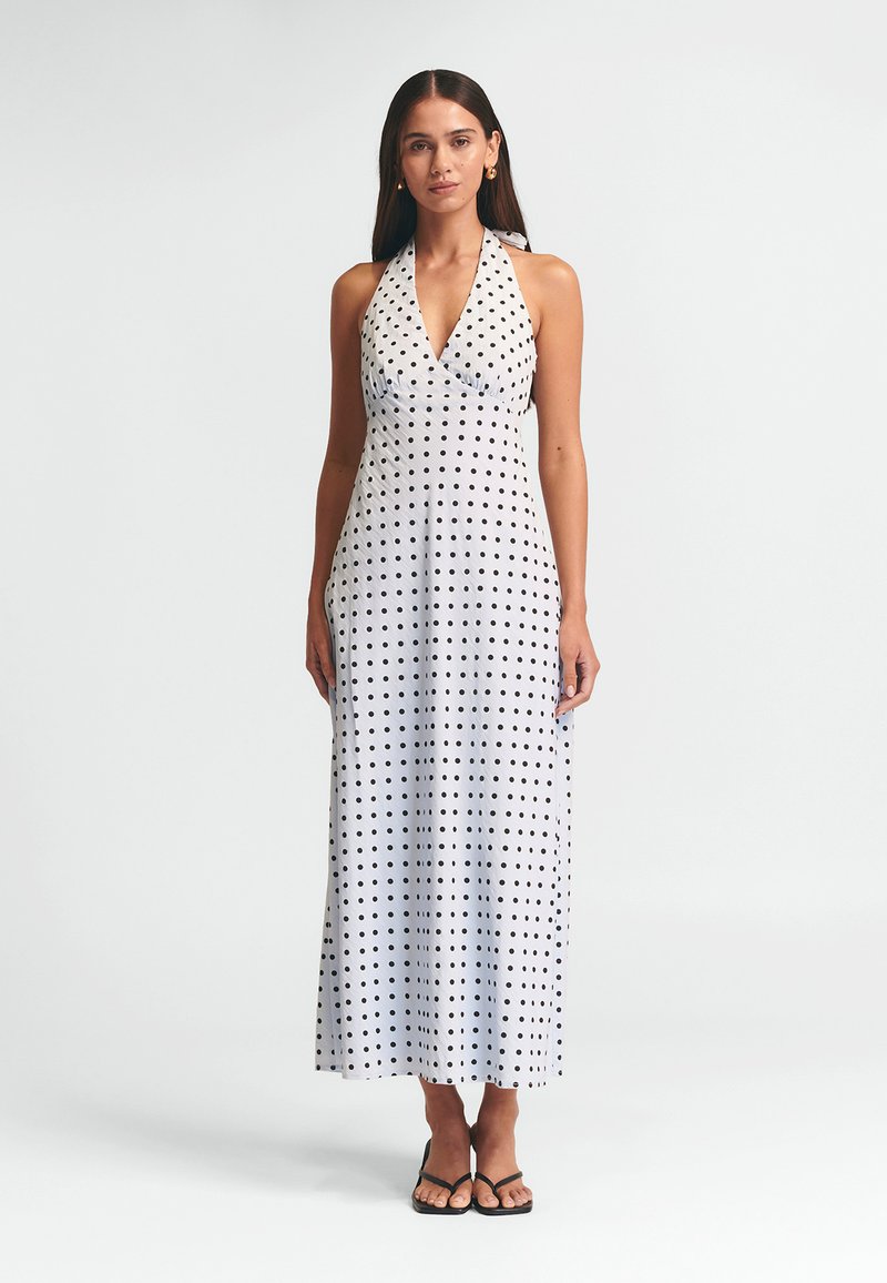 Šaty bez rukávov s halter výstrihom, vyrobené z ľahkej látky; sú pokryté čiernymi bodkami na bielom pozadí; dlhé až po zem s priliehavým korzetom.