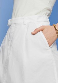 Falda de algodón blanca con bolsillos, con un corte recto y una textura sutil. Se aprecian los pasadores para cinturón y una cinturilla limpia.