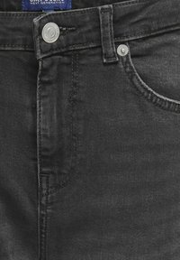 Svart denimjeans har en klassisk femficksdesign, med metallnitar, sydda sömmar och en slät yta.