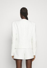 Costume blanc texturé avec un motif en losange, comprenant un blazer structuré et un short sur mesure. Le matériau possède un léger éclat.