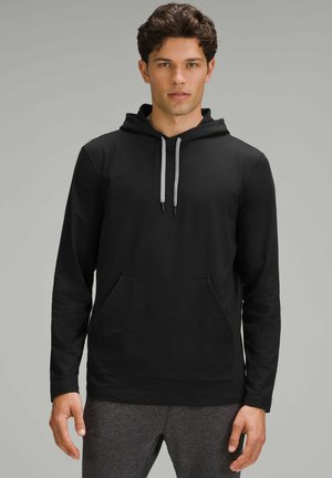 Felpa nera a maniche lunghe con tasca frontale, cappuccio con coulisse e dettagli grigi, e una texture del tessuto liscia. Abbinata a pantaloni grigi.
