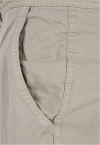Beige Baumwollshorts mit einer Seitentasche und doppelter Nahtdetail. Der Stoff hat eine glatte Textur und einen leichten Glanz.