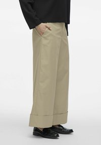 Beige vide bukser i en glat tekstur, med sidelommer og dobbelt foldet kant. Bruges sammen med sorte loafers.