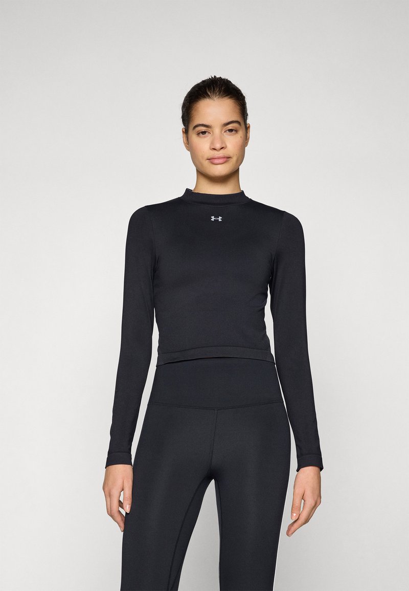 Črna športna majica z dolgimi rokavi in visokim izrezom, prilegajoča se zasnova, gladka tkanina in logotip Under Armour na prsih, v kombinaciji z ujemajočimi se leggins hlačami.